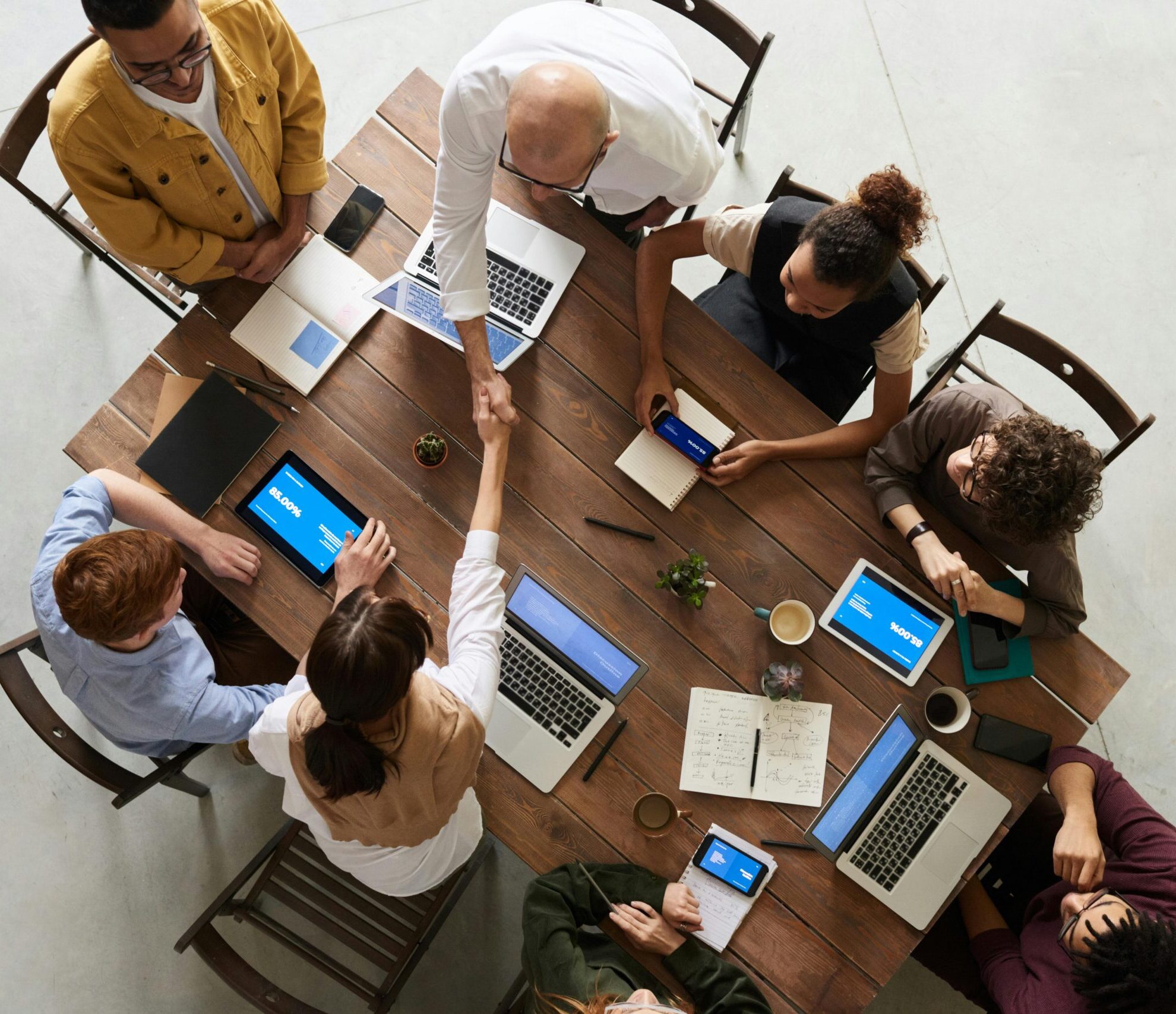 Top view of a diverse team collaborating in an office setting with laptops and tablets, promoting cooperation.