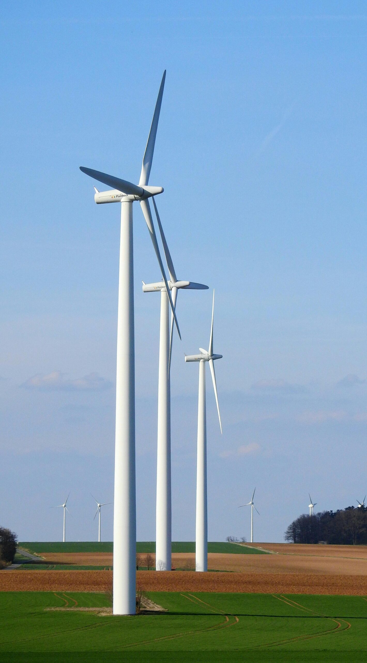 Row of wind turbines in a rural area, generating renewable energy under a blue sky.